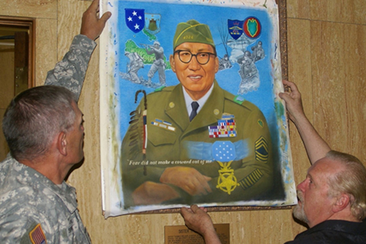 Two men look at a painting of a service member.
