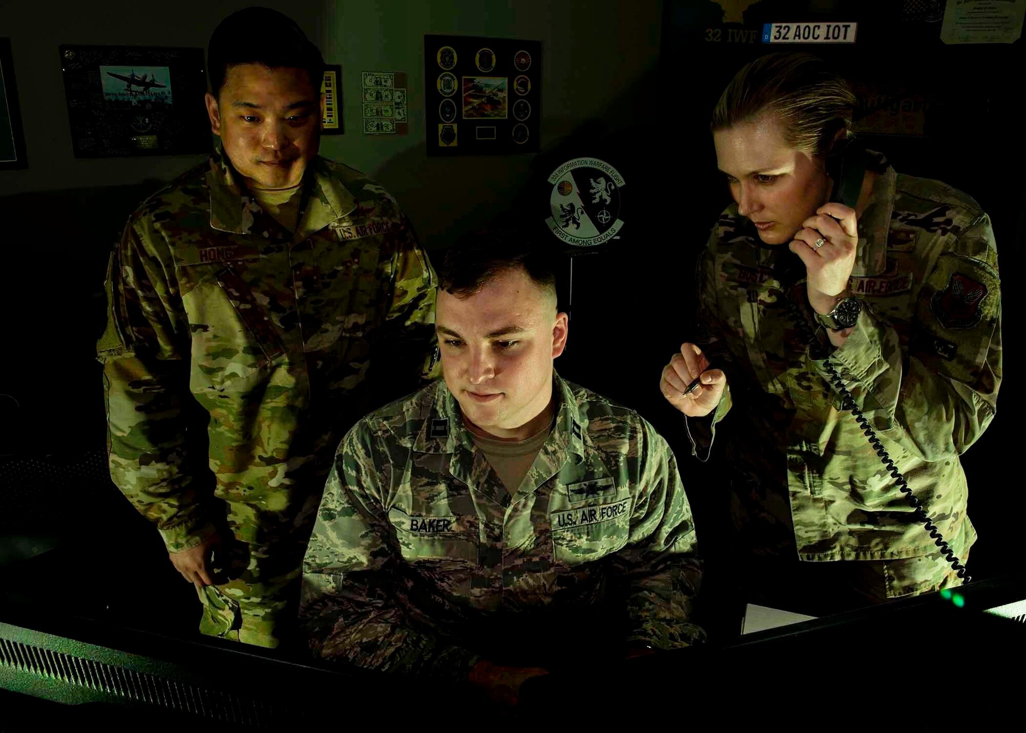 Two Airmen look at a computer while one speaks on the phone.