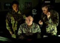 Two Airmen look at a computer while one speaks on the phone.