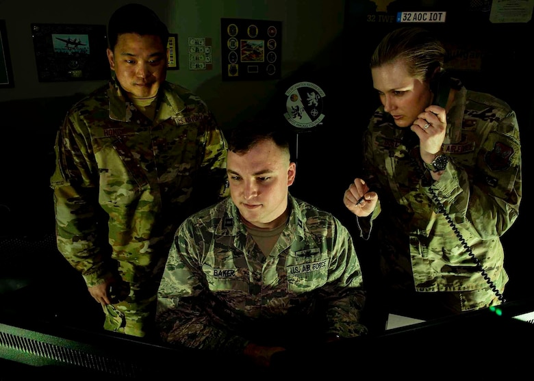 Two Airmen look at a computer while one speaks on the phone.