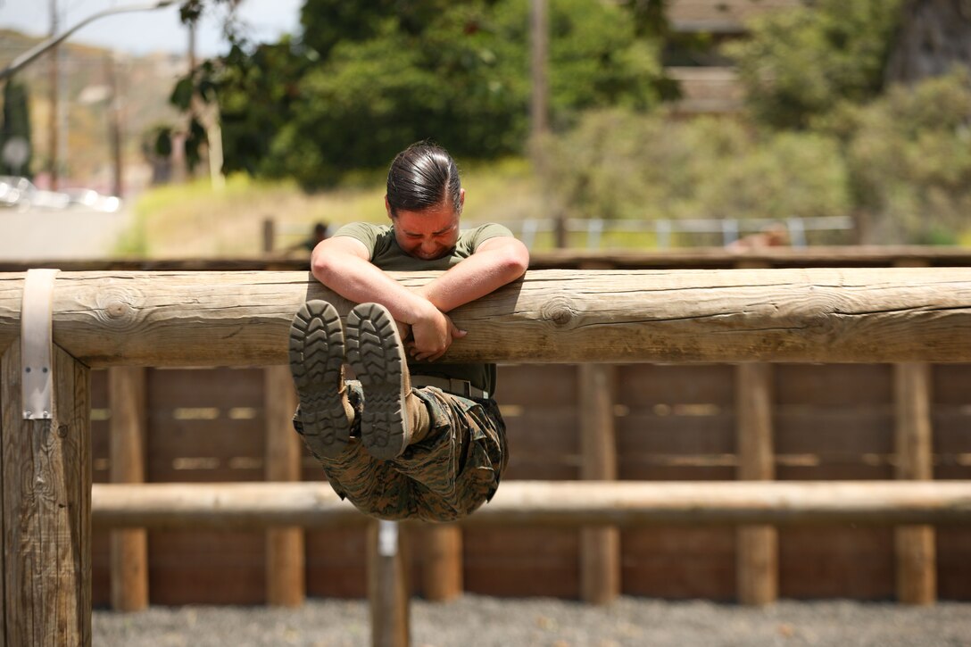 A midshipman struggles to get over a log on an obstacle course.