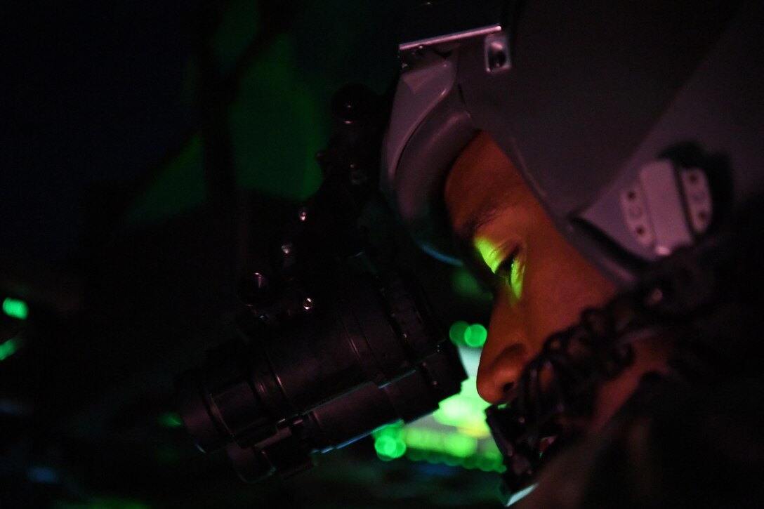 A pilot in a cockpit wearing a helmet looks through a scope.