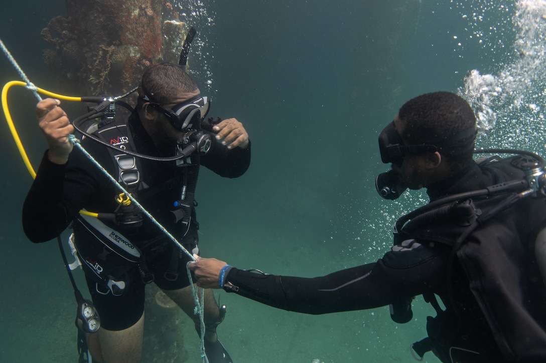 Caribbean divers signal to the surface as they perform a jetty search during Exercise TRADEWINDS 19 in St. Vincent and the Grenadines