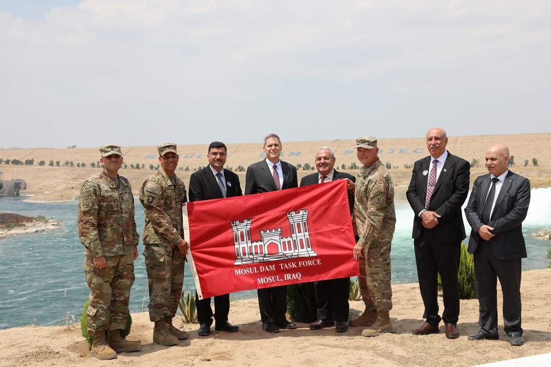 Members of the U.S. Army Corps of Engineers, the U.S. Ambassador to Iraq, and members of the Government of Iraq celebrate the completion of the Mosul Dam Task Force mission in Iraq by holding up the MDTF Mission Flag on the banks of the Tigris River in front of the dam. Pictured left to right are: U.S. Army Corps of Engineers Transatlantic Division Command Sergeant Major Randolph Delapena, TAD Commander Col. Mark Quander, Iraq Minister of Water Resources Director General Mahdi Rashid, U.S. Ambassador to Iraq Matthew H. Tueller, Iraq Minister of Water Resources Jamal al-Adili, Mosul Dam Task Force Commander Col. Philip Secrist, Mosul Dam Project Manager Riyadh Ali, and Iraq Director General of Planning and Follow-up Jamal Mohsin. The dignitaries were visiting the MDTF on June 15, 2019, for a ceremony commemorating the completion the Mosul Dam Project, which started in 2016 as a joint project among the Iraq Ministry of Water Resources, the U.S. Army Corps of Engineers, and Italian Company Trevi S.p.A. in an effort to stabilize the infrastructure of the Mosul Dam. The Dam is the largest in Iraq and the fourth largest in the Middle East. It supplies water, hydropower, irrigation and flood control to the region.