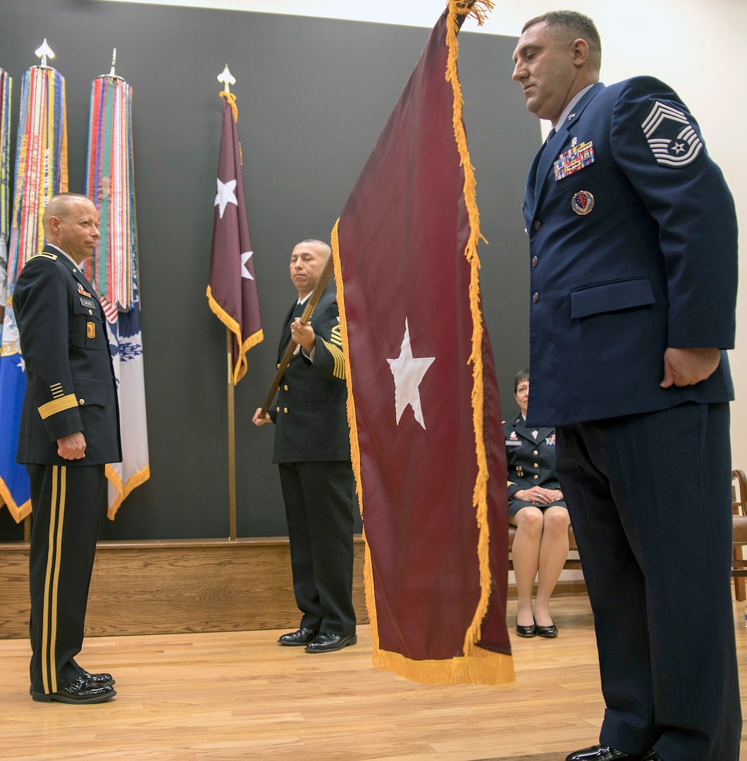 Chief Master Sgt. Joshua Barr, Medical Education and Training Campus command chief, and Senior Chief Petty Officer Victor Flores, METC senior enlisted advisor, uncase and present the Army Medical Department brigadier general (maroon) general officer flag to Brig. Gen. Jack Davis during a ceremony in METC’s Anderson Hall Auditorium at Joint Base San Antonio-Fort Sam Houston June 7.