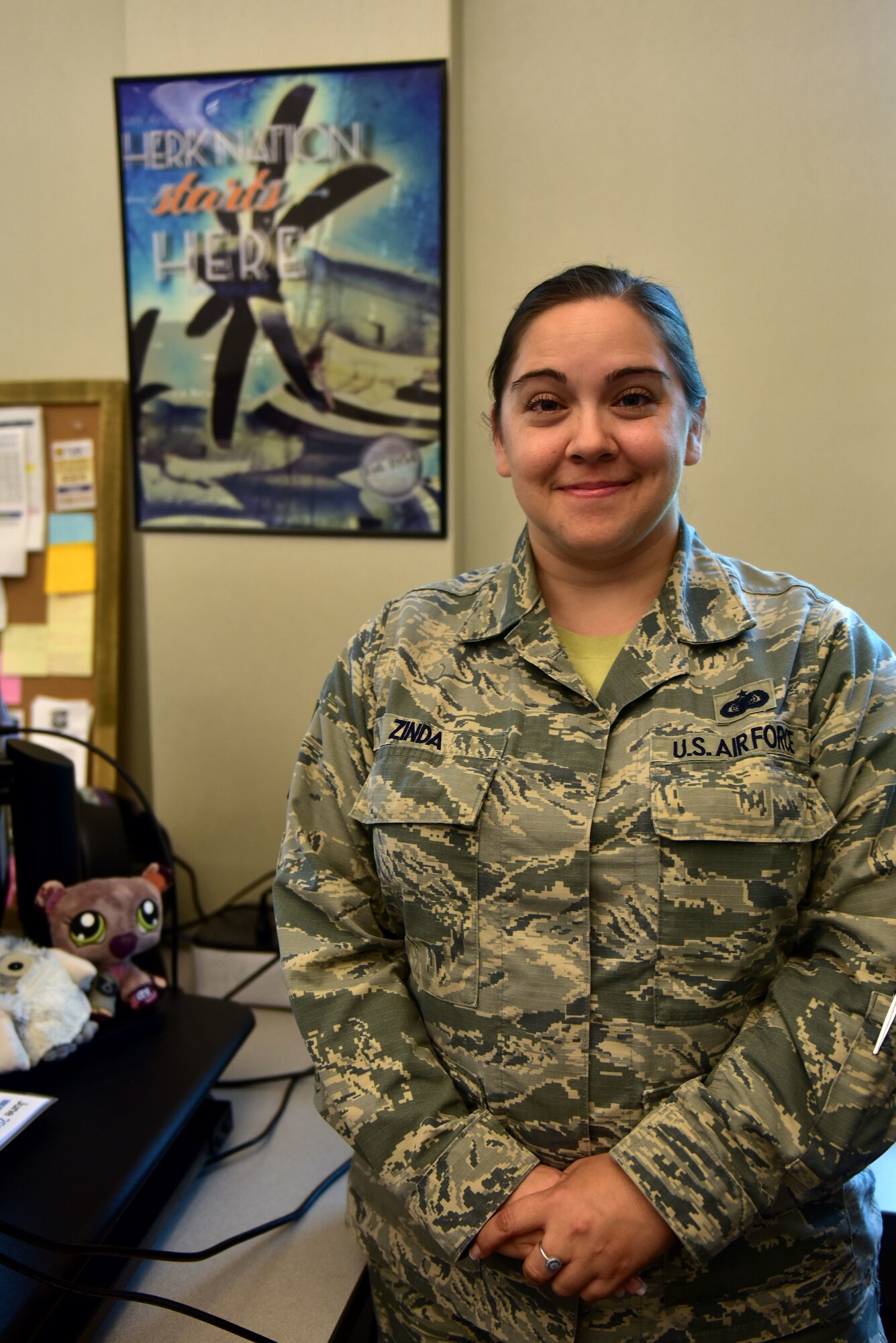 A woman stands in front of a desk in the Airman Battle Uniform.