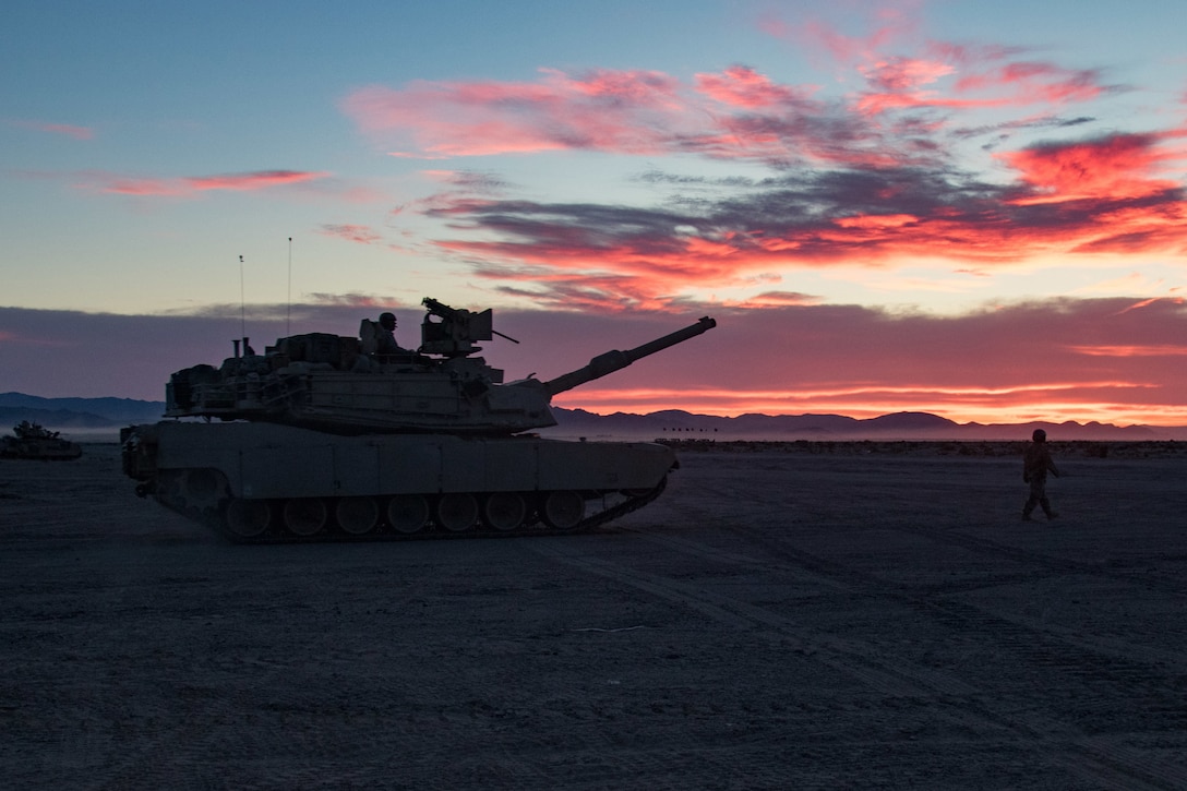 A tank sits outside as dawn breaks with scattered red clouds overhead.