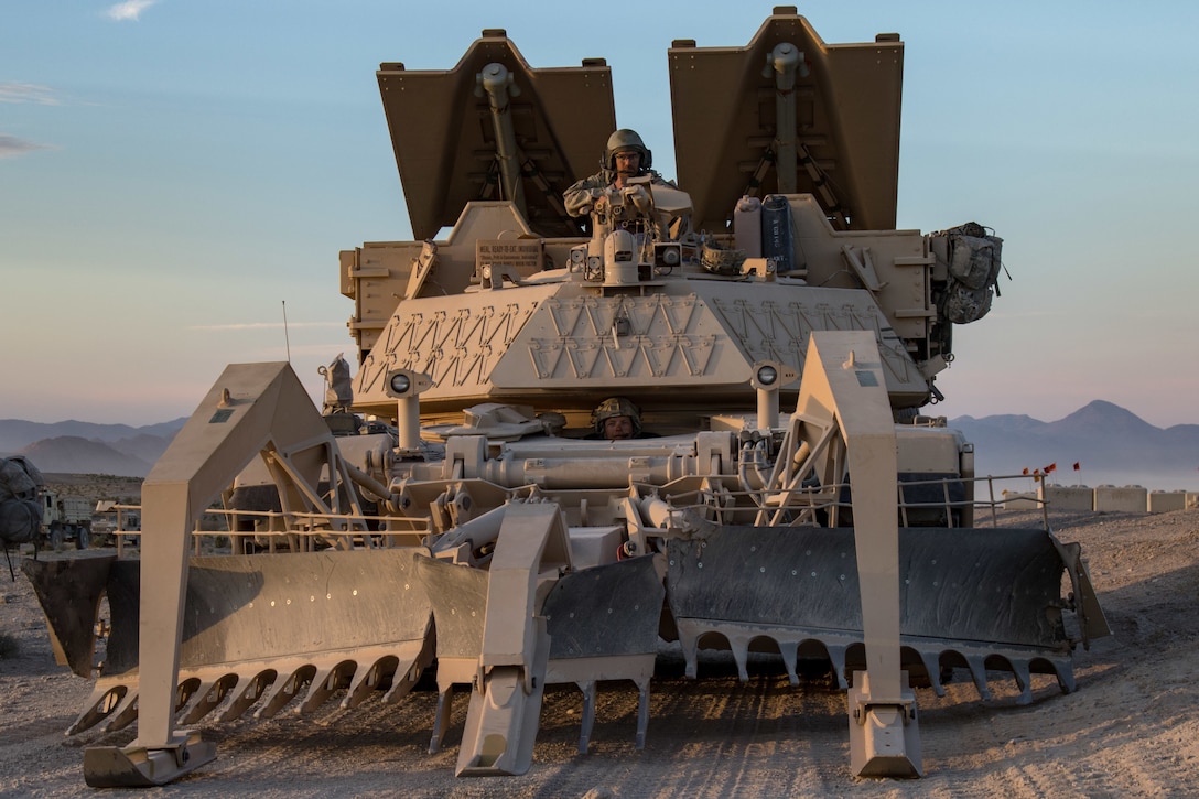 A soldier sits at the top of a huge military vehicle in the desert.