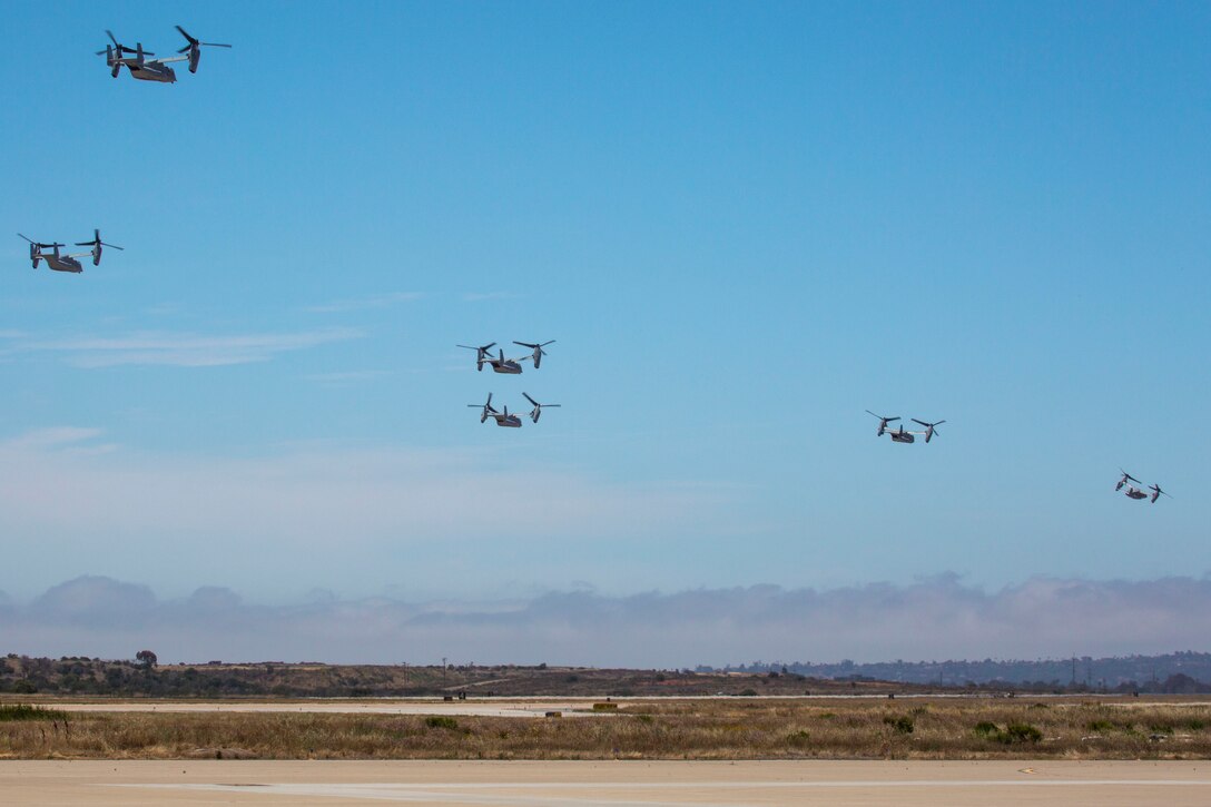 Six tiltrotor aircraft fly over a flat desert.