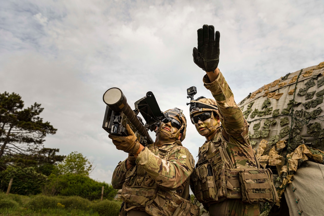 On soldier holds a missile over his shoulder while another soldier points in the distance.