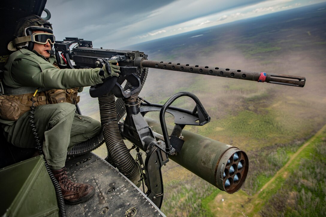 A Marine mans a weapon mounted to an aircraft in flight.