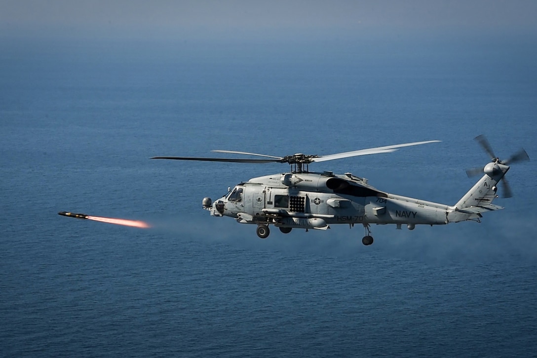 A helicopter fires a missile while flying over the sea.