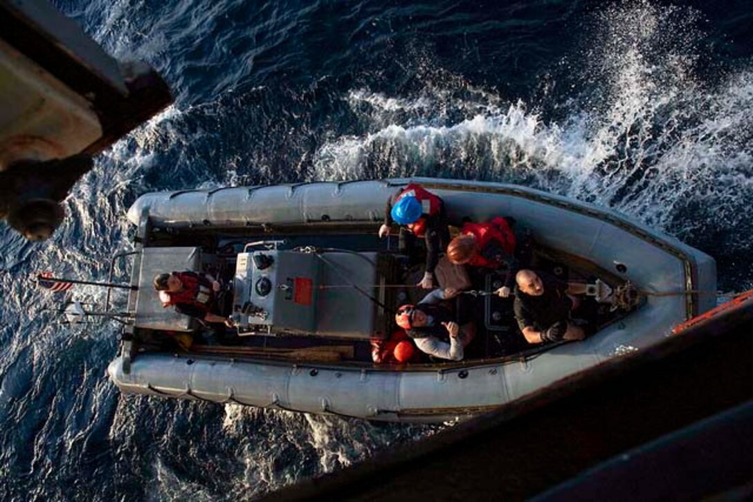 An overhead shot of sailors sit inside a small inflatable boat.