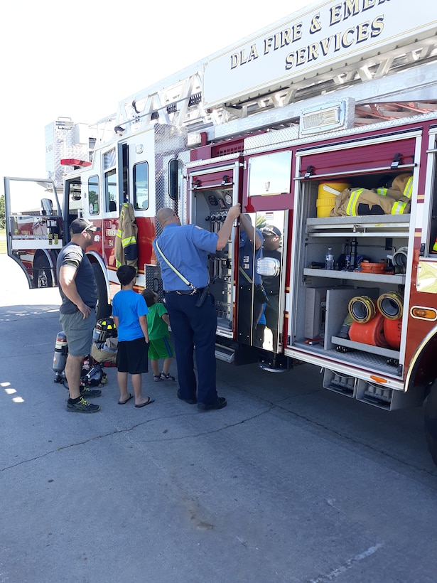 A man, woman and two children look at the side features of a fire truck