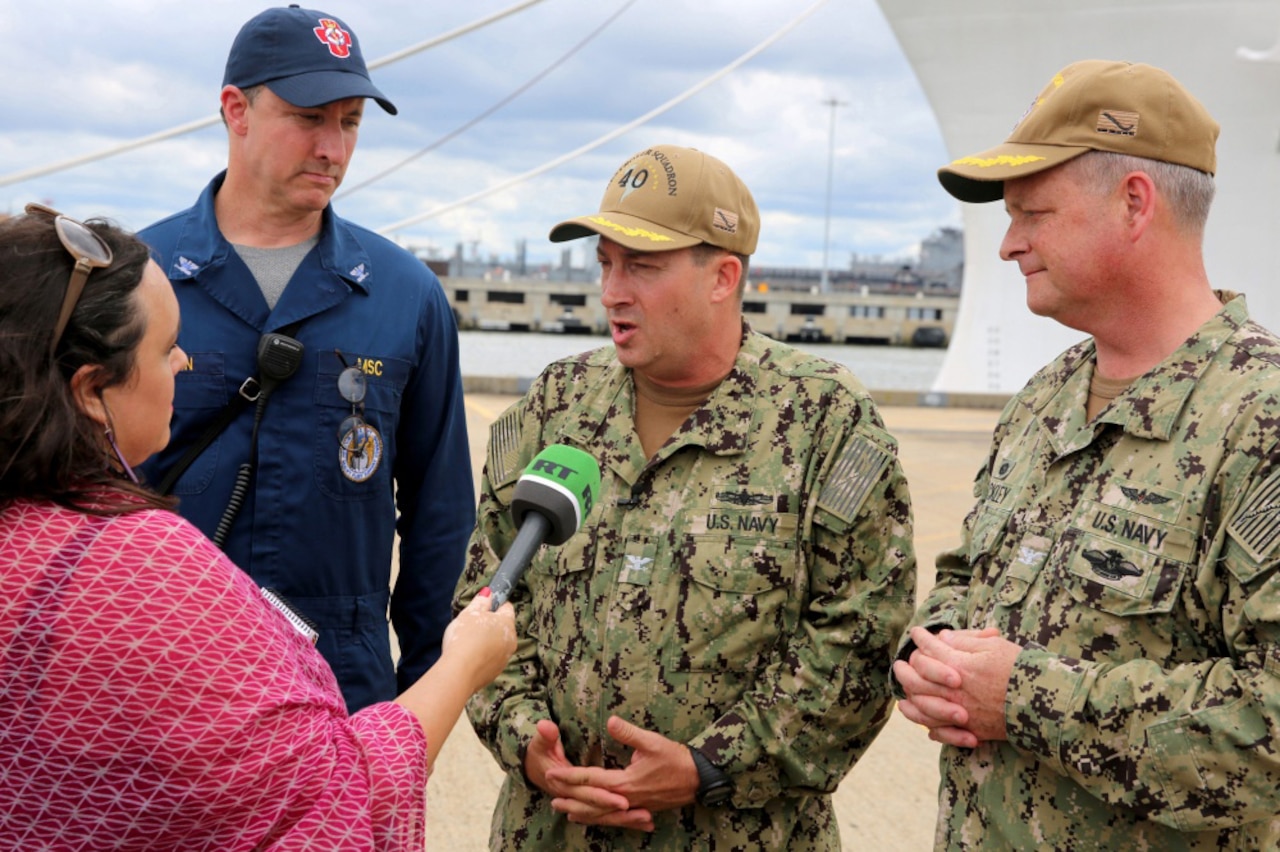 A reporter interviews three Navy officers in uniform.