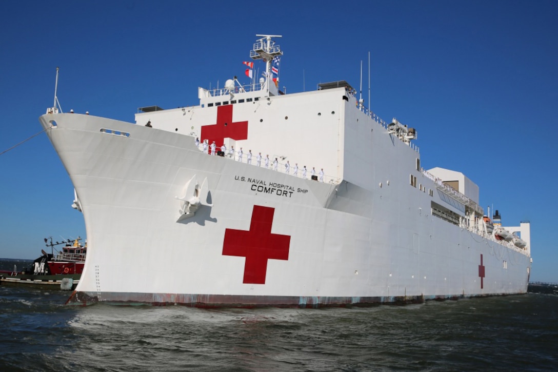A white hospital ship with red cross markings moves through the water.