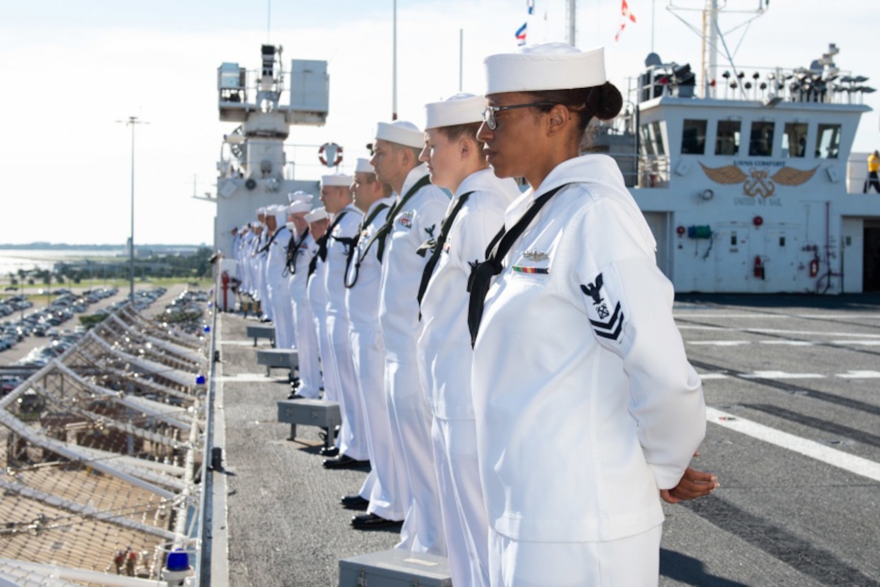 Sailors in white uniforms line the rail of a hospital ship.