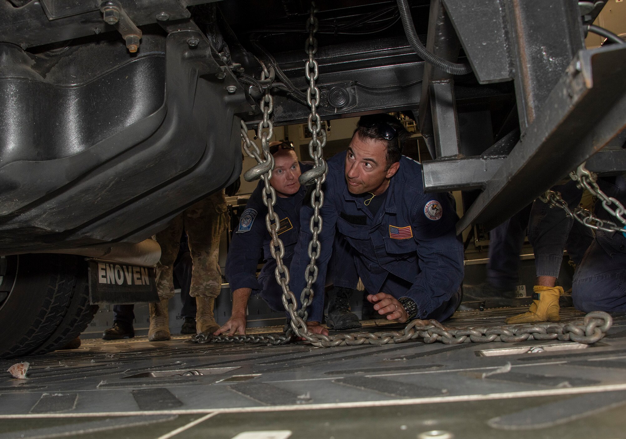 Liam McGregor, left, transportation manager and Matt Gonzales, California Urban Search and Rescue Task Force 7 transportation specialist, use a chain to secure an equipment transport trailer to the deck of a C-17 Globemaster III during a joint inspection and logistics drill conducted with 60th Aerial Port Squadron personnel June 13, 2019 at Travis Air Force Base, California. The annual training helps members of CA TF-7 learn about the process, governing and directives and ensures cargo is safe before loading onto an aircraft.  (U.S. Air Force photo by Heide Couch)