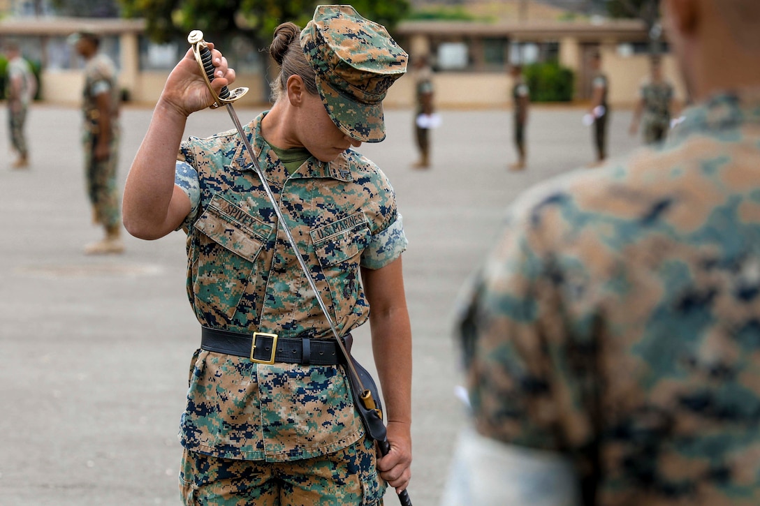 A Marine puts a sword back into a sheath on her hip.