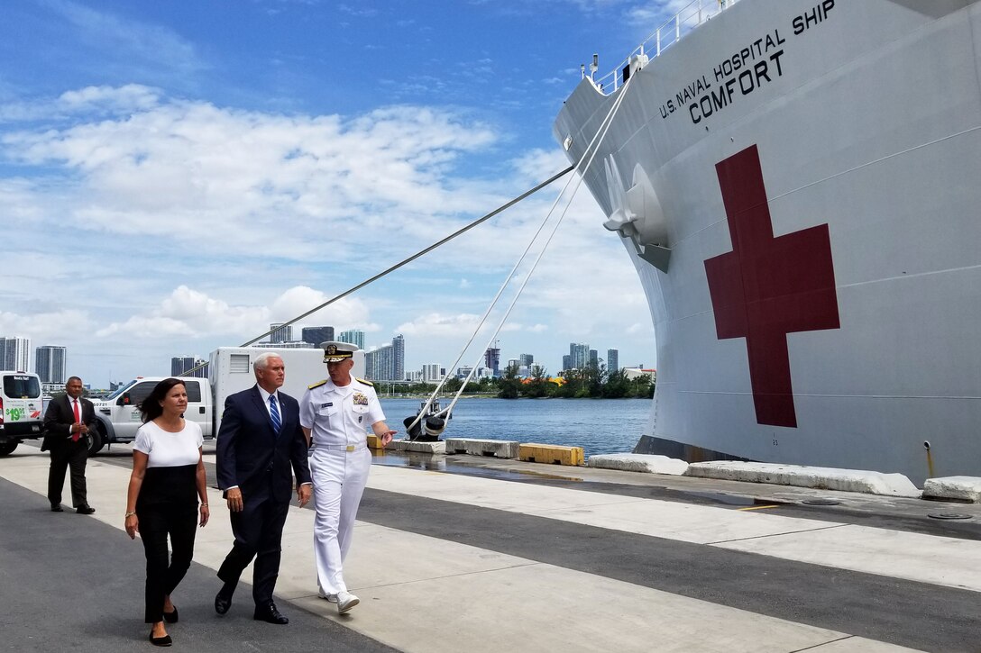 Two men and a woman walk along the pier next to a hospital ship.