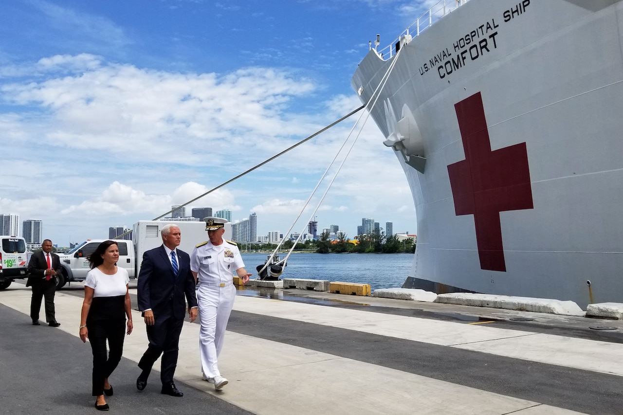 Two men and a woman walk along the pier next to a hospital ship.