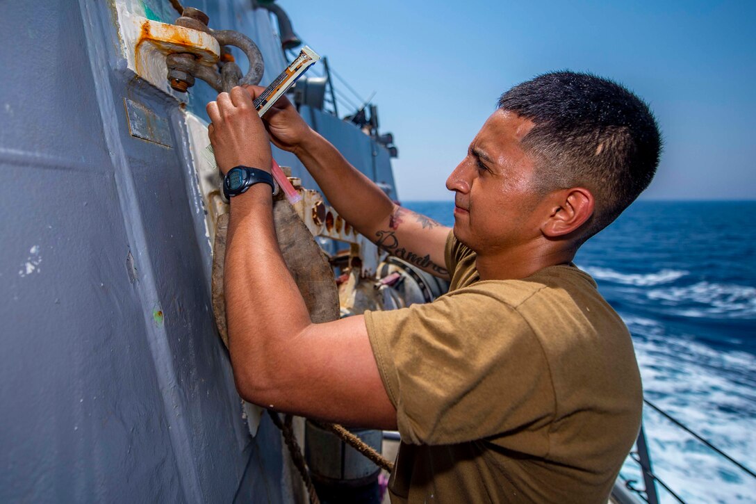 A sailor ties lights to the side of a ship.