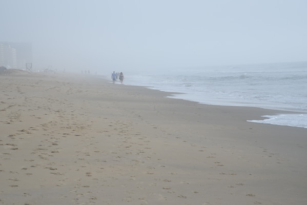 Two people walk along a foggy beach