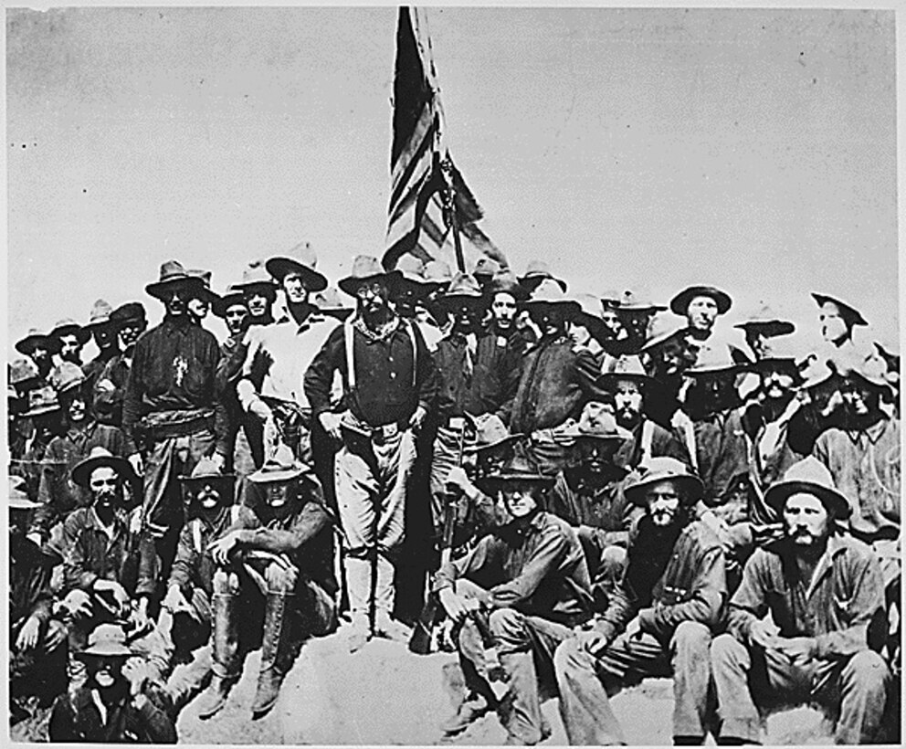 Several soldiers wearing wide-brimmed hats stand around a U.S. flag with then-Army Col. Theodore Roosevelt.