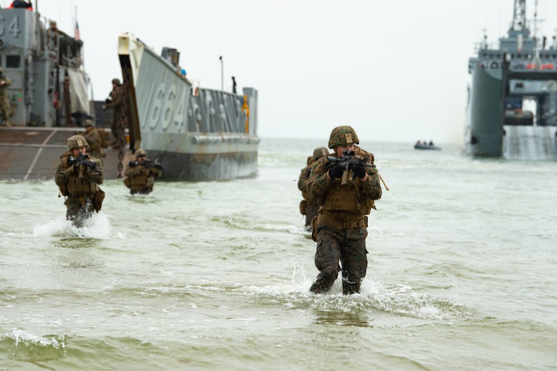 Armed Marines move onshore from a watercraft.