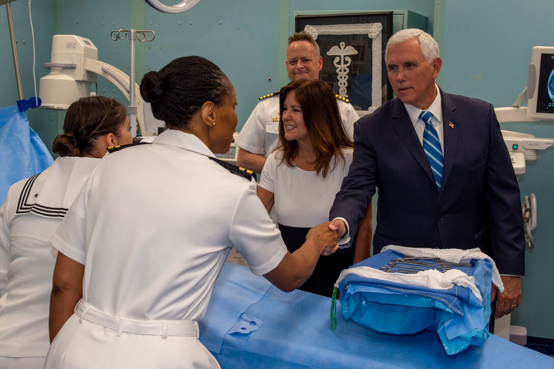 The vice president and second lady shake hands with sailors across a hospital bed aboard a ship.
