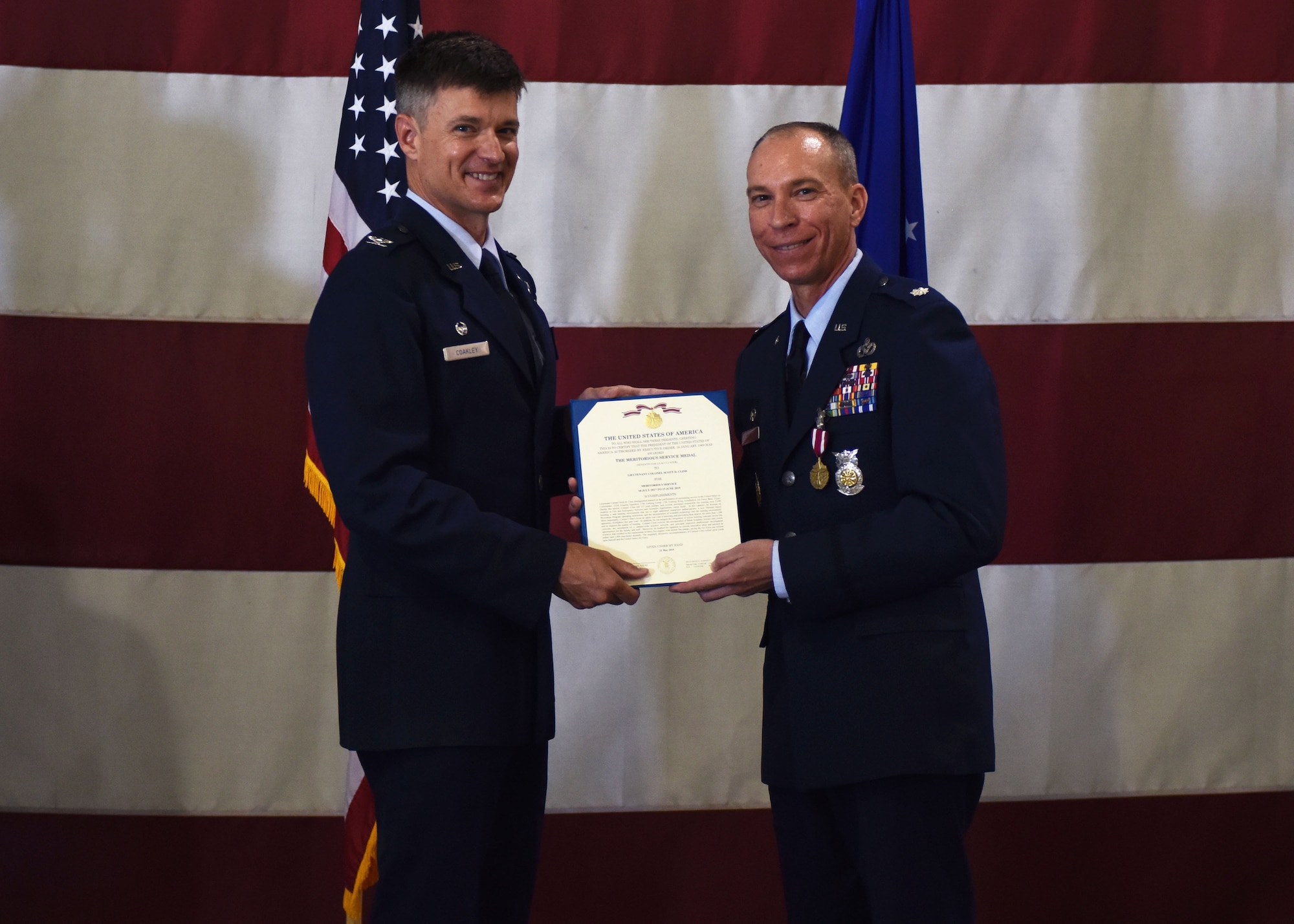 U.S. Air Force Col. Thomas Coakley, 17th Training Group commander, presents Lt. Col. Scott Cline, 312th Training Squadron outgoing commander, the certificate for Cline’s Meritorious Service Medal during the change of command ceremony at the Louis F. Garland Department of Defense Fire Academy High Bay on Goodfellow Air Force Base, Texas, June 19, 2019. Cline received the medal for leading a joint team of military and civilian personnel who trained over 2,600 fire emergency services and scientific applications students each year. (U.S. Air Force photo by Airman 1st Class Zachary Chapman/Released)