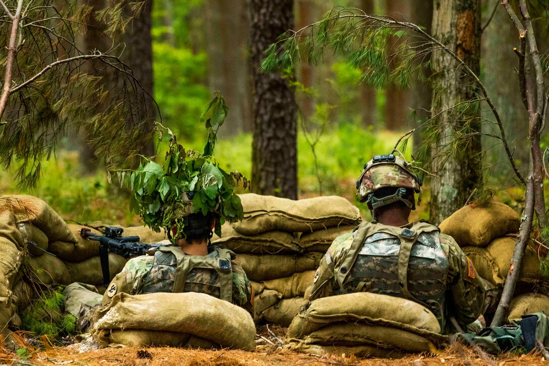 Two soldiers sit behind a bunker made of sandbags.