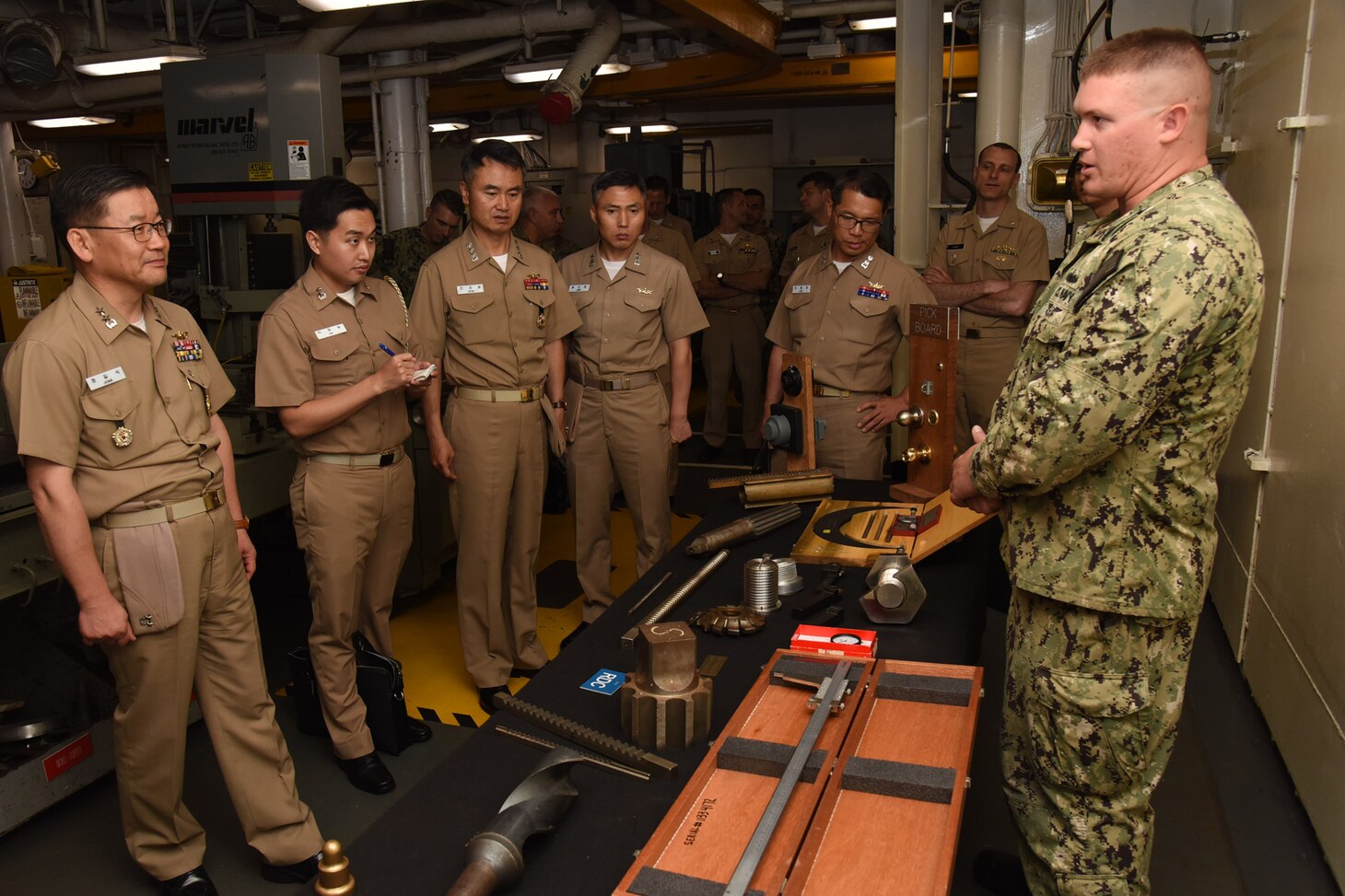 APRA HARBOR, Guam (June 18, 2019) Machinery Repairman 2nd Class Marcus Flake gives a presentation to Rear Adm. Jung II Shik, commander of the Republic of Korea Navy Submarine Force, left, and other Republic of Korea Navy personnel during a tour of the machine shop on the submarine tender USS Emory S. Land (AS 39), June 18. Rear Adm. Jung is in Guam attending the 49th annual Submarine Warfare Committee meeting. During the meeting, U.S. and Korean officials discuss interoperability, the planning of combined training opportunities, and continued development of integrated anti-submarine warfare plans.