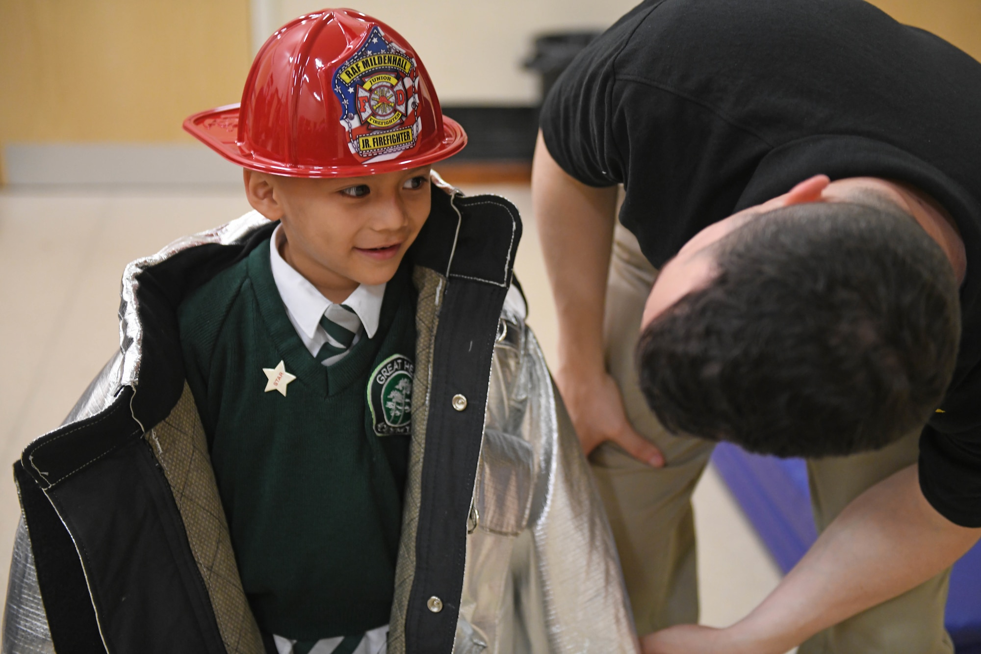 U.S. Air Force Tech. Sgt. Daniel Howard, 100th Civil Engineer Squadron firefighter, helps a student put on firefighting equipment at Great Heath Academy, Mildenhall, England, June 19, 2019. The firefighters showed students how they use their gear and allowed them to try it on. (U.S. Air Force photo by Senior Airman Luke Milano)
