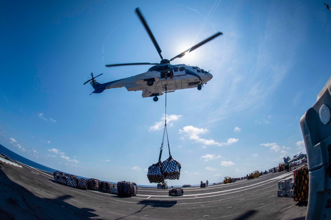 A helicopter lowers a box of supplies onto a ship.