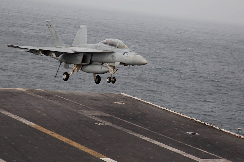 A fighter jet lands on the deck of an aircraft carrier.