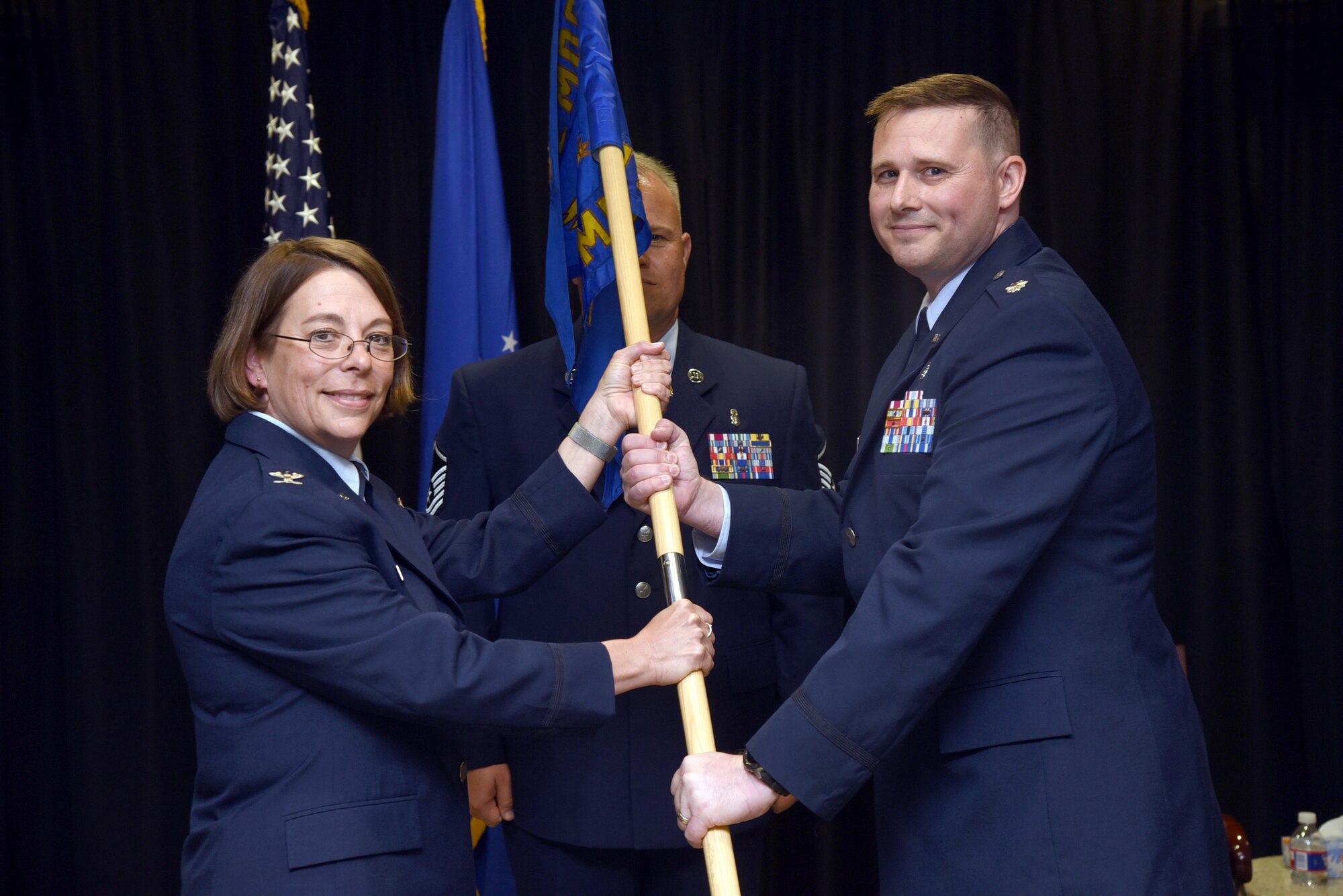 72nd Medical Group Commander Col. Jennifer Trinkle presents the guidon of the 72nd Medical Operations Squadron to the new commander, Lt. Col. Colin Burchfield during a formal change of command ceremony June 13. Lt. Col. Randall Stevens relinquished command of the squadron he led for the past two years. (U.S. Air Force photo/Kelly White)