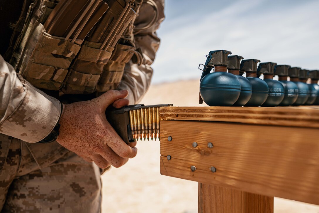 A Marine loads ammo into a clip using leverage from a table topped with grenades.