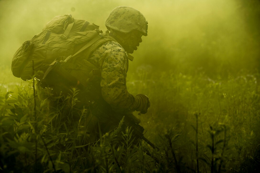 A Marine with a backpack walks through a field shrouded in yellow smoke.