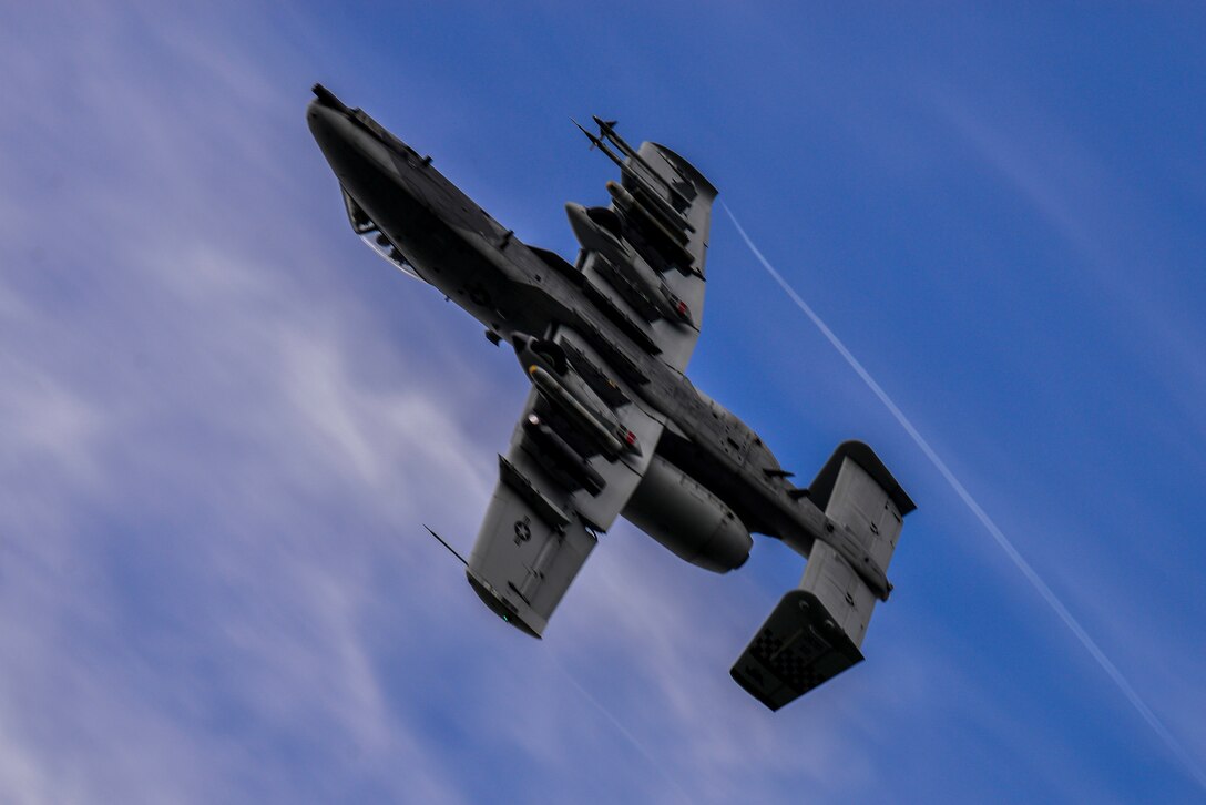 An aircraft flies nearly upside down through the sky.