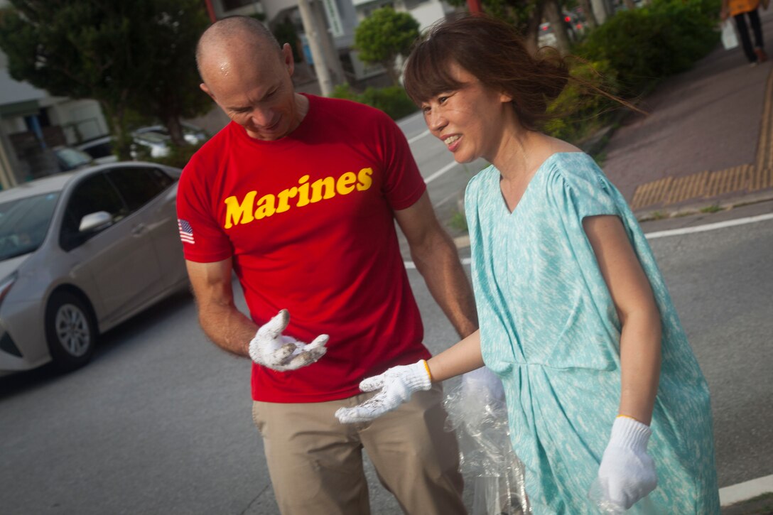 U.S. Marine Corps Col. David Steele, the commanding officer for Marine Corps Air Station Futenma, and Kasumi Tonogami, a residential worker for the island of Okinawa, compare the thorns on their gloves after picking up garbage during the cleanup around the Ginowa convention area, Okinawa, Japan, June 19, 2019.