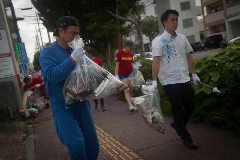 Okinawa residents followed by U.S. Marines carry bags filled with garbage they had picked up during the cleanup around the Ginowa convention area, Okinawa, Japan, June 19, 2019.