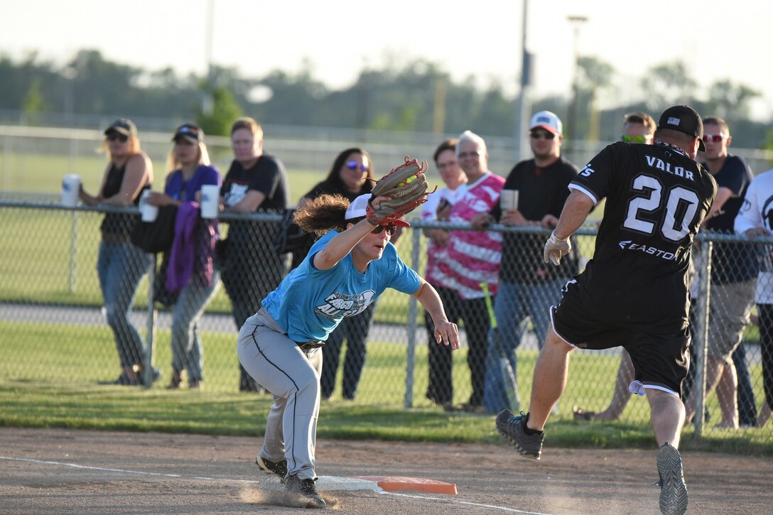 Master Sgt. Brandi Grossman, of the 119th Security Forces Squadron, stretches to catch a softball at first base as retired Chief Master Sgt. Randall Raper is called out during a charity softball game at the softball complex north of Fargo, N.D., June 14, 2019.