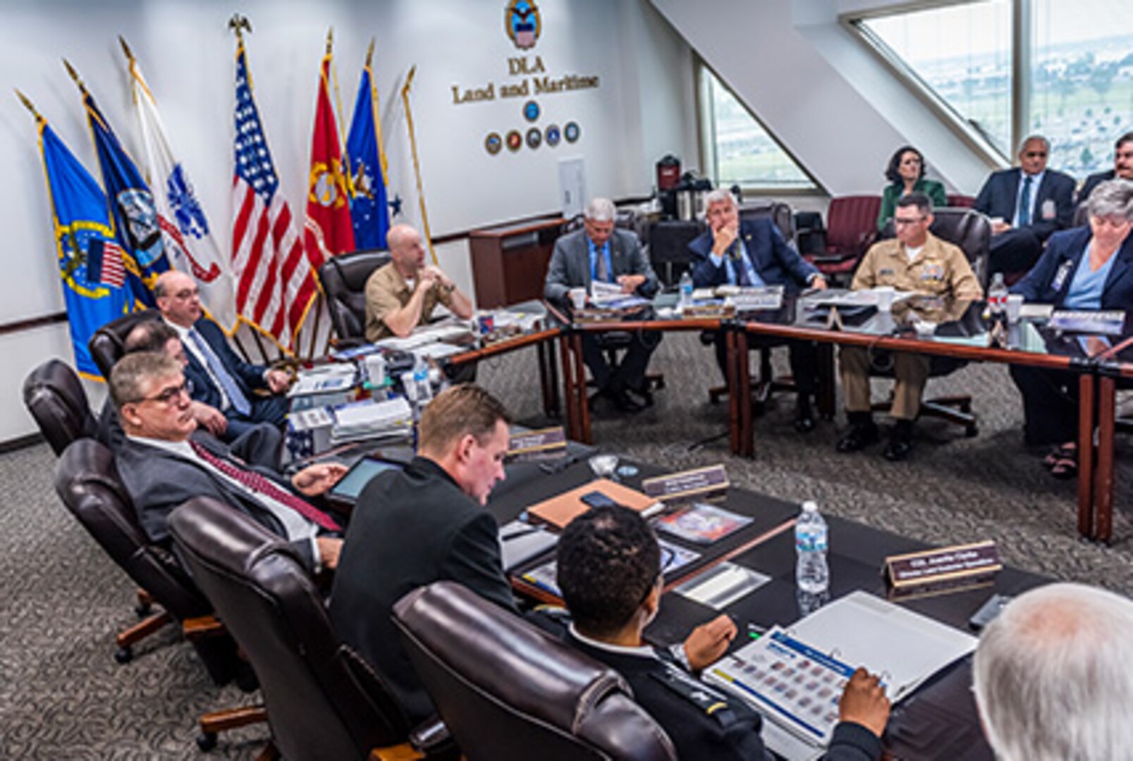 People sit around a u-shaped table with a flag display in the background