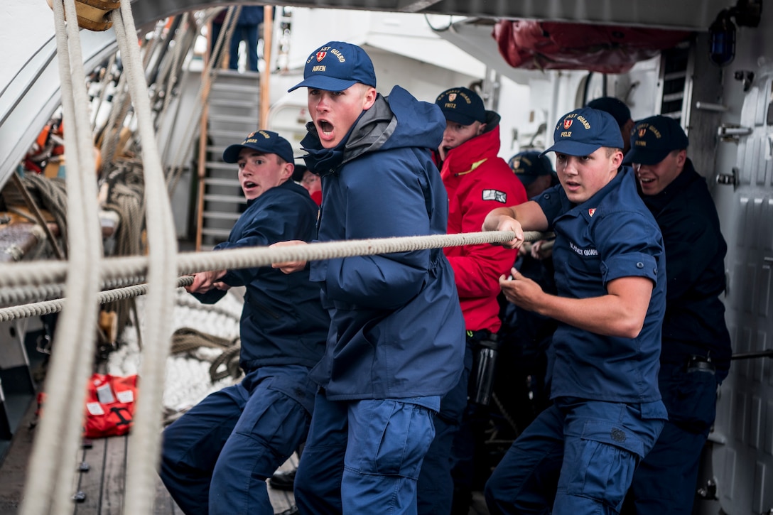 A group of men pull on a set of ropes aboard a ship.