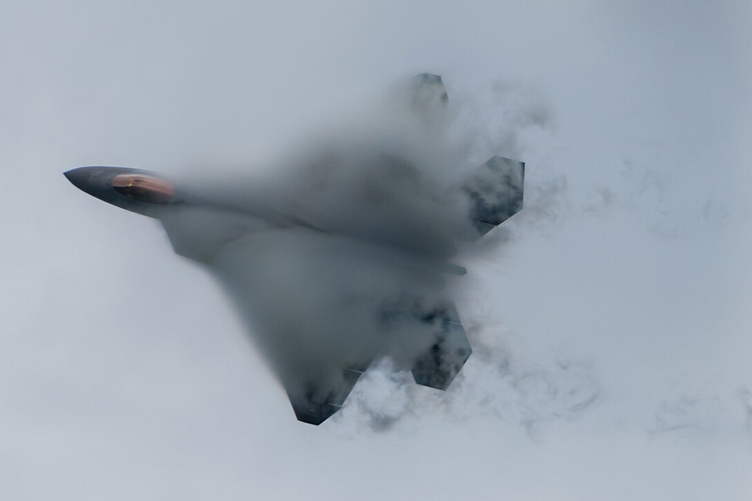 A military fighter jet flies through the air with smoke around it.