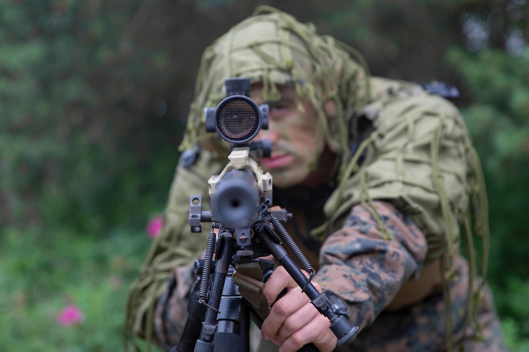 A Marine in camouflage aims his weapon at the camera.