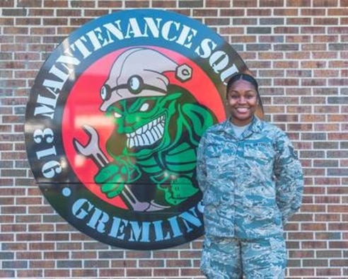 A woman in the Airman Battle Uniform stands in front of a sign.