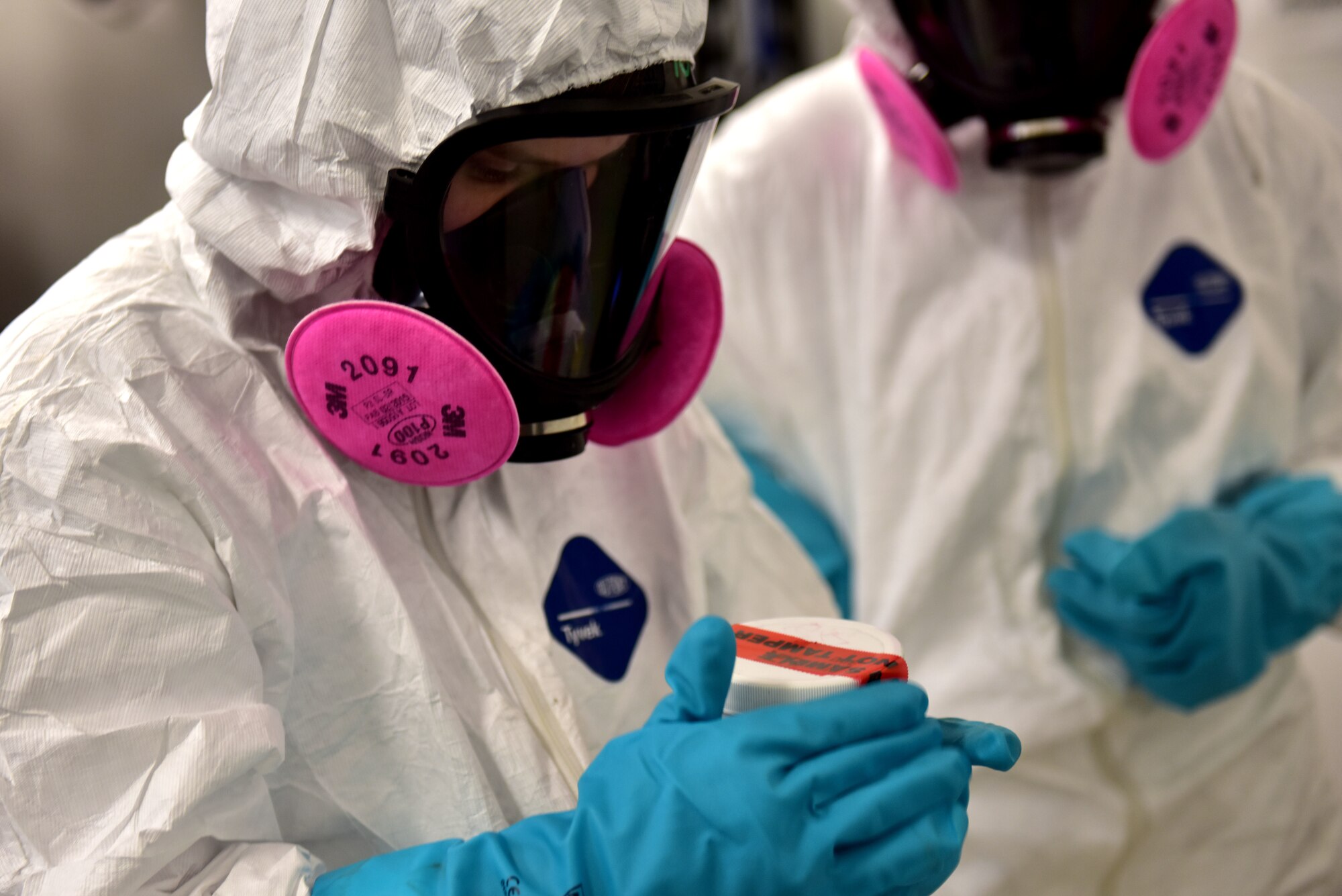 Two people in protective suits seal a container.