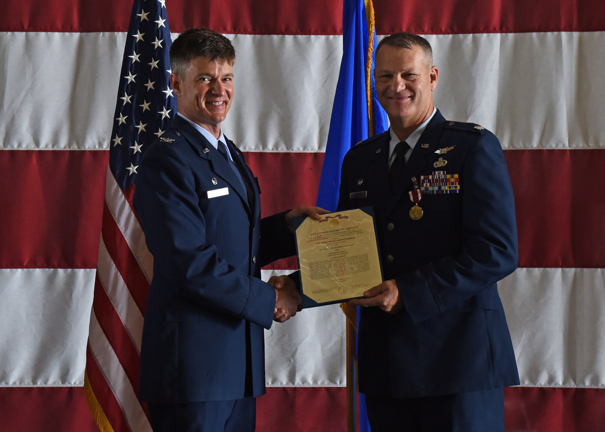 U.S. Air Force Col. Thomas Coakley, 17th Training Group commander, presents Lt. Col. Robert Kammerer, 316th Training Squadron outgoing commander, the certificate for Kammerer’s Meritorious Service Medal during the change of command ceremony at the Louis F. Garland Department of Defense Fire Academy High Bay on Goodfellow Air Force Base, Texas, June 21, 2019. Kammerer was responsible for training over 6,400 Army, Navy, Air Force, Marine, and Coast Guard intelligence warriors annually, in communication signals intelligence, electronic intelligence, fusion analysis, cryptologic language analysis, and human intelligence. (U.S. Air Force photo by Airman 1st Class Zachary Chapman/Released)